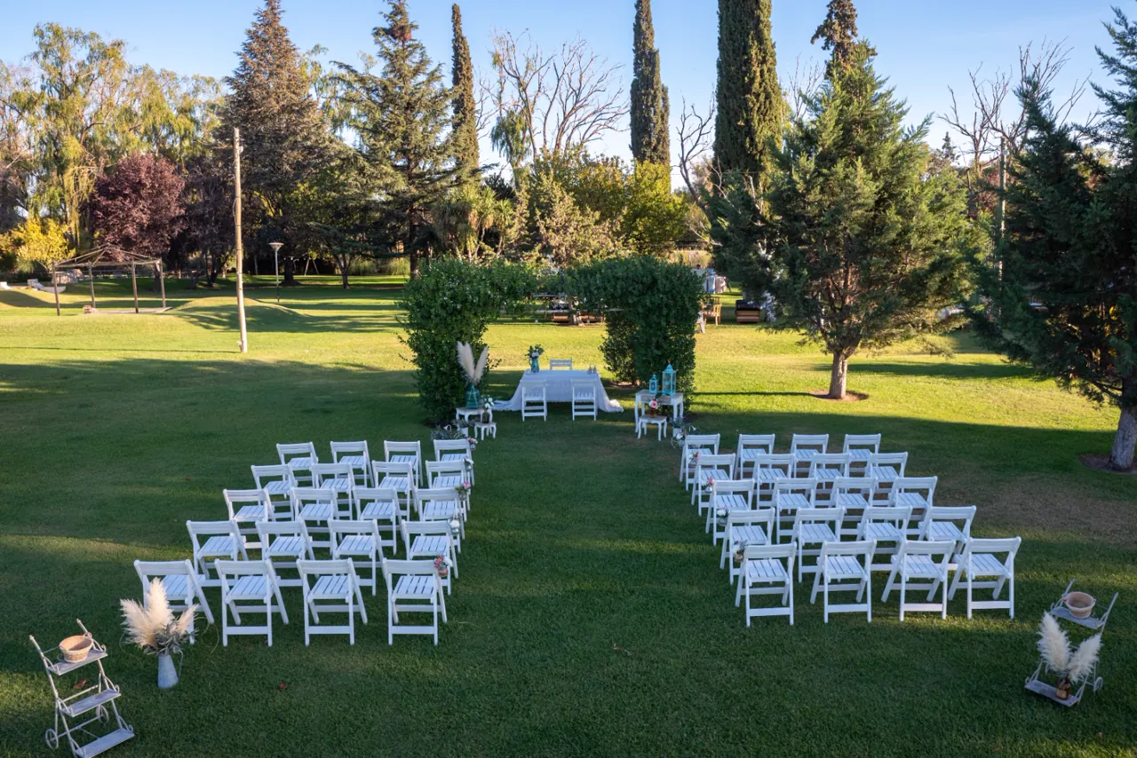 Ceremonia montada en el parque con sillas blancas y arco de verde