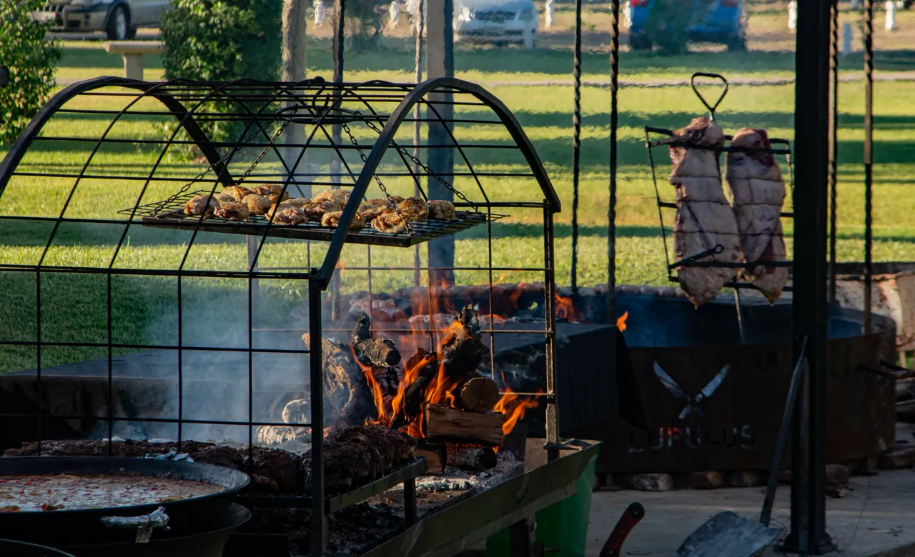 Carnes asándose en la parrilla de arco junto al fuego