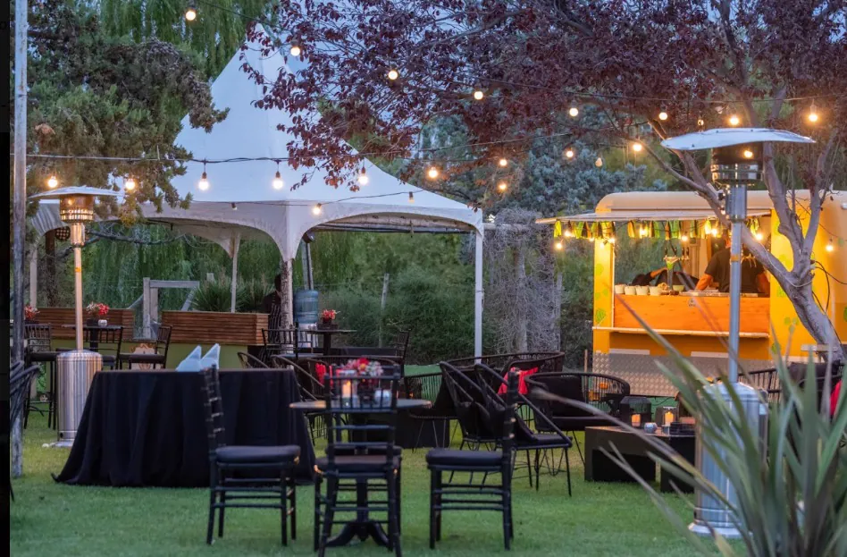 Carpa y barra de food truck con mesas vestidas de negro en el jardín