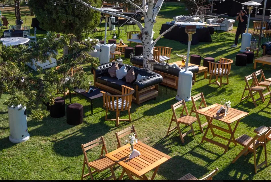 Vista del jardín con livings y mesas de madera montados entre los árboles