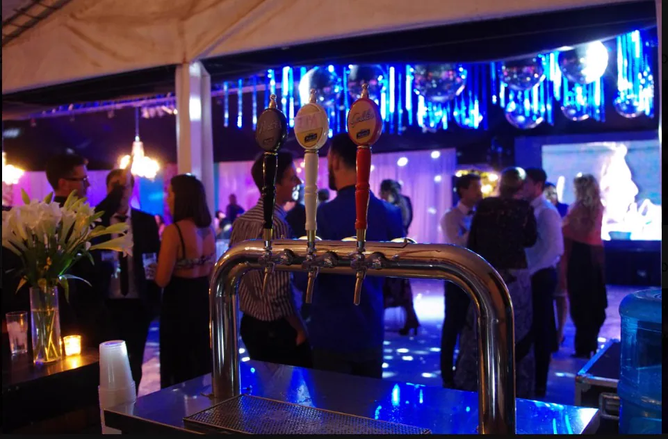 Barra con choperas y la pista iluminada de azul durante una fiesta nocturna