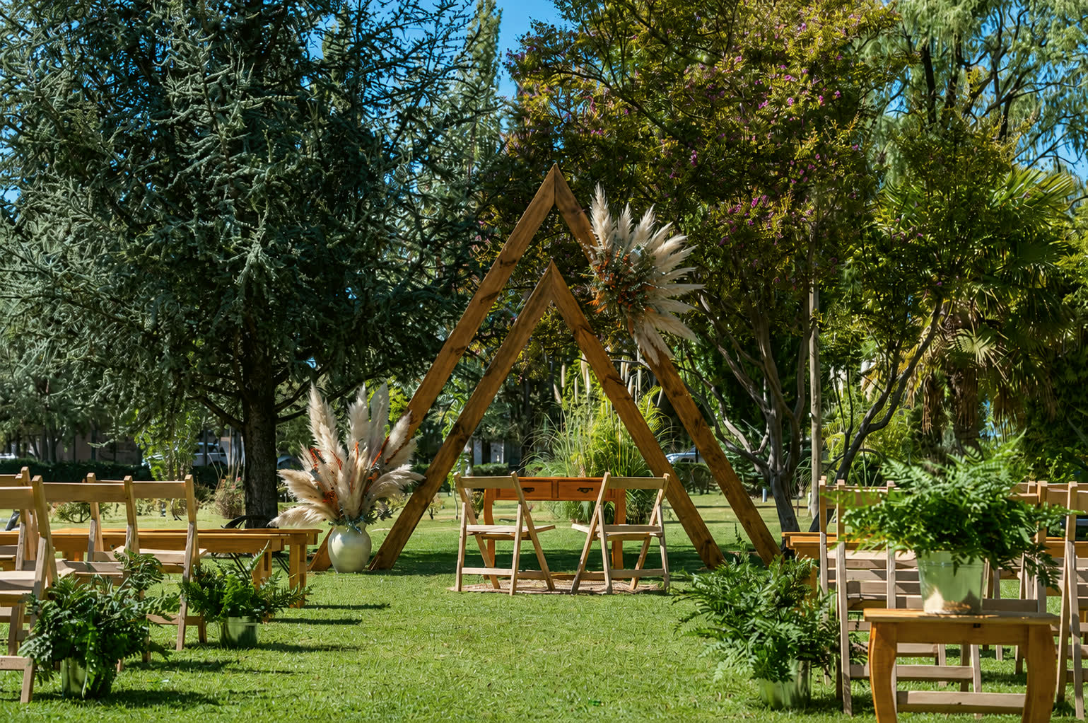 Ceremonia de día en el jardín con arcos triangulares de madera decorados con plumas de cortadera