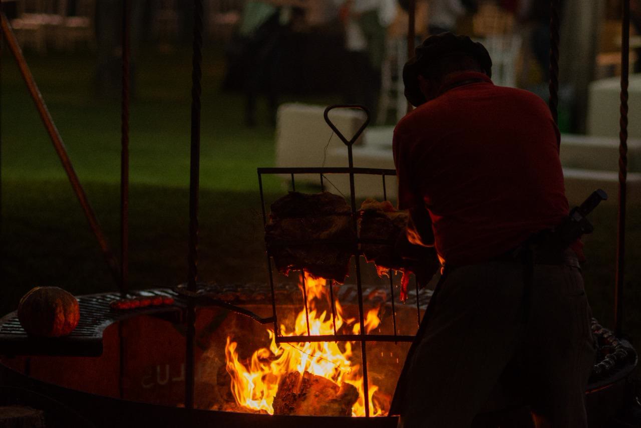 Parrillero cocinando cortes de carne sobre el fuego de un fogón durante un evento nocturno